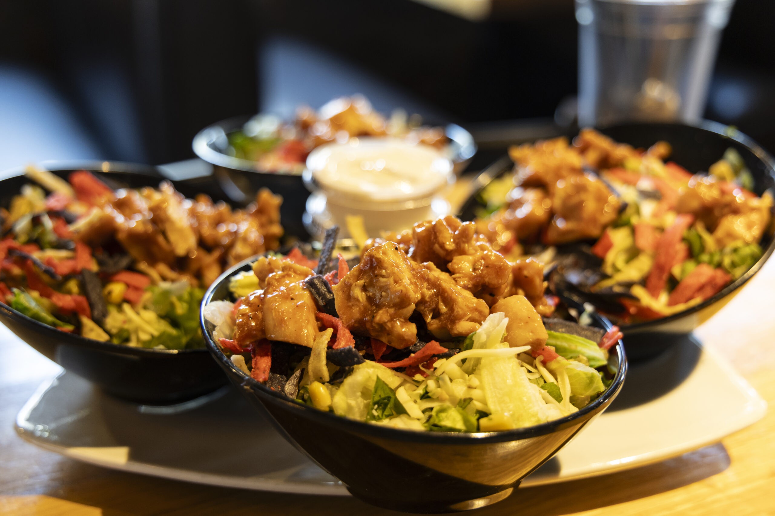 A platter with four bowls of salad topped with pieces of chicken.