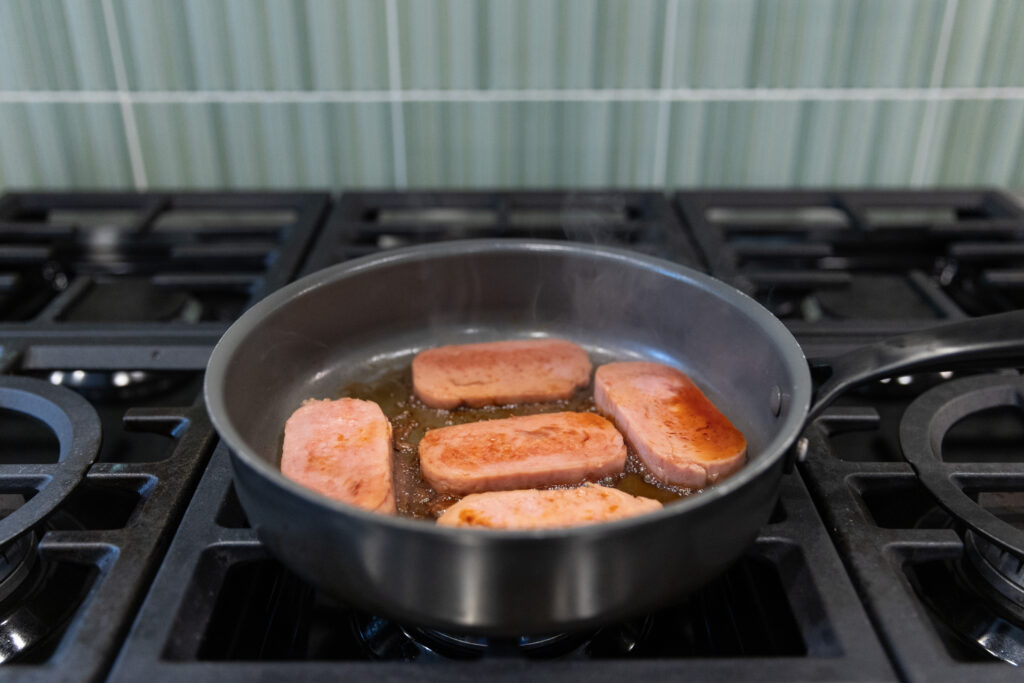 Five slices of spam fry in a pan