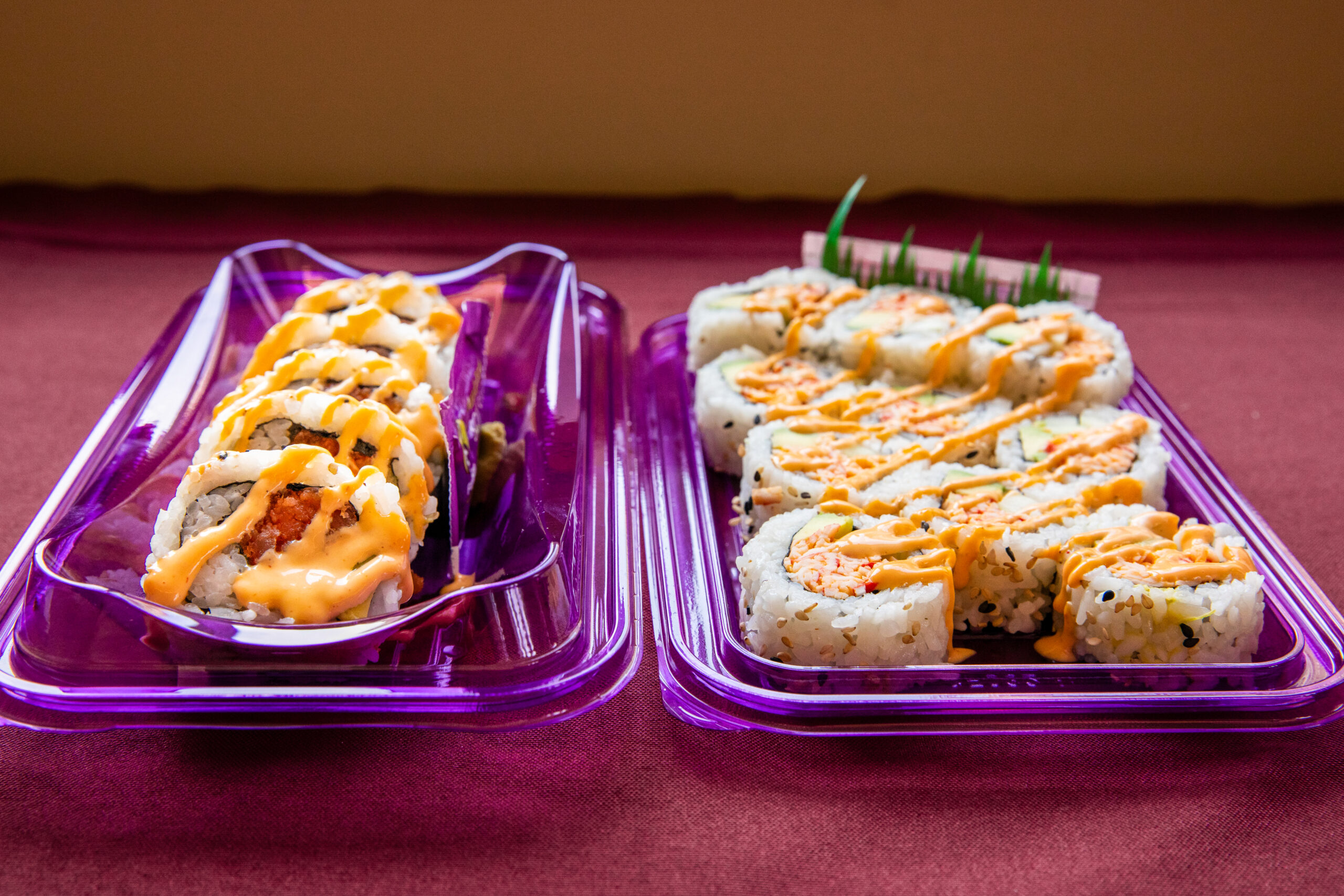 A spicy tuna roll and a spicy California roll, both in purple plastic trays