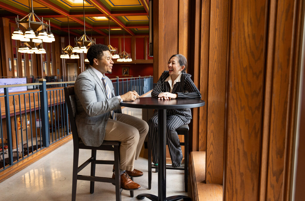 Blake Comeaux and Dr. G talking at a table in the DUC adjacent to large windows.